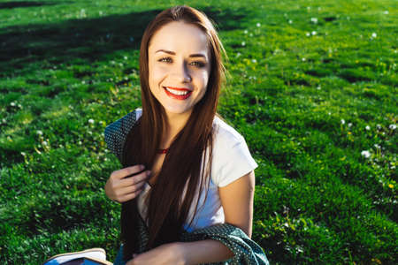 Cute smiling woman sitting on grass at summer dayの写真素材