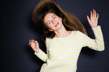 Happy teenage girl jumping, warm clothes, black background