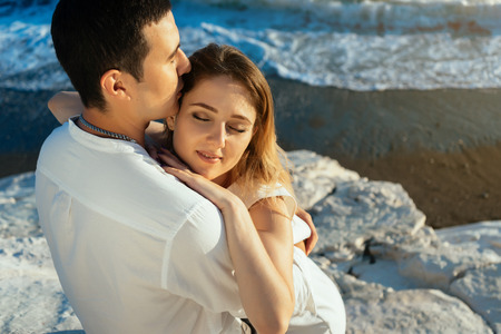 beautiful tender couple sitting on stones at the seaside and huggingの写真素材