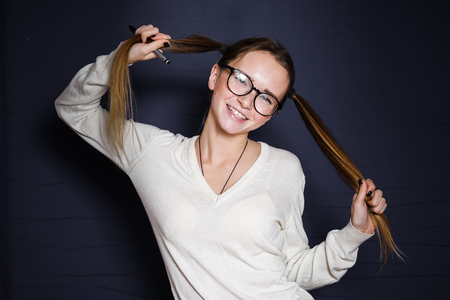 young smiling girl holding herself at the braids with a pen in her hands on a black backgroundの写真素材