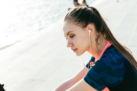 beautiful girl in sports clothes pensively sitting on the seashoreの写真素材