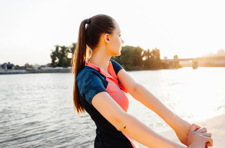 girl on the river bank warming up before jogging at sunsetの写真素材