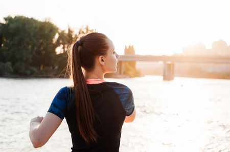 girl doing warm-up near river bank at sunsetの写真素材
