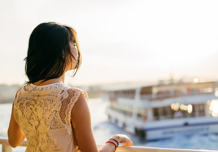 A girl travels by ship on the water at sunset, stands with her back, enjoys the sunsetの写真素材