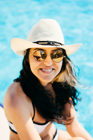Woman in a hat and sunglasses smiling near pool in hotelの写真素材