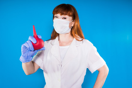 a girl in medical clothes and wearing a mask looks at the camera and holds a medical device in her handsの写真素材