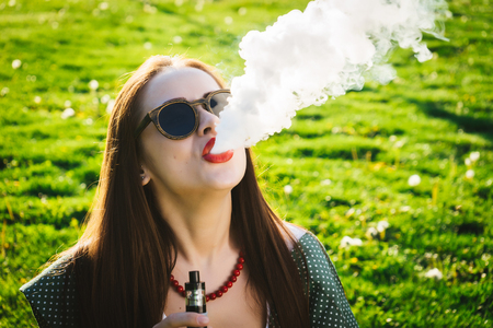 Happy fashion smiling Woman in sunglasses smoking vape on street, smoke
