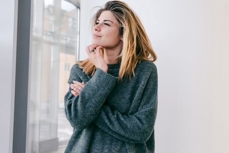 beautiful cute girl in gray sweater smiling and looking out the windowの写真素材