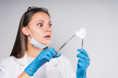 girl nurse holding in hands with tweezers cotton wool looking at her wonderinglyの写真素材