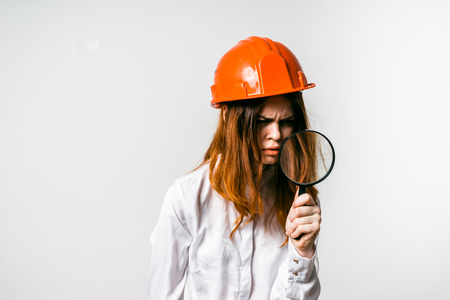 girl in an orange construction helmet looks angrily at the magnifierの写真素材