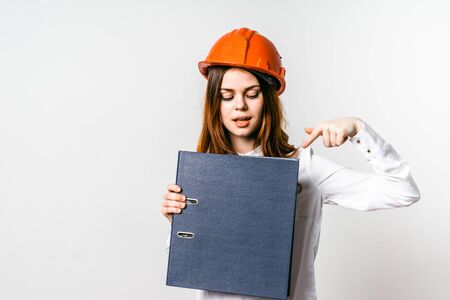 girl in orange construction helmet smiling showing at folder in her handsの写真素材