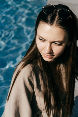 girl in sunglasses sits by the blue water in the sun, portraitの写真素材
