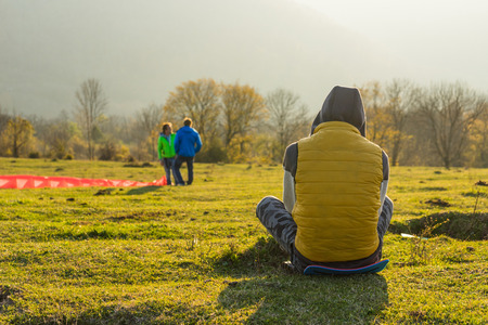 the man is sitting on the ground in a yellow jacket and hoodの写真素材