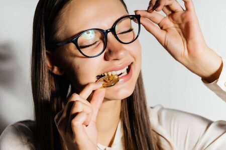 a nice girl with glasses is trying to taste a gold coin. Money, wealth