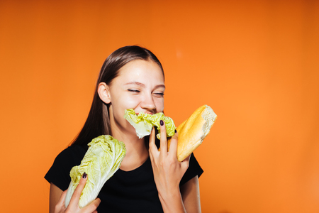 the girl holds a cabbage and a loaf in her hands. Girl chewing cabbage, isolated on orange backgroundの写真素材
