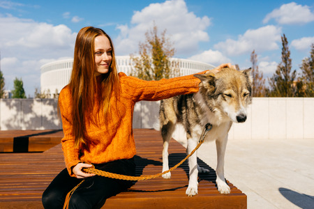 young red-haired girl smiling, sitting on a wooden bench with her dog