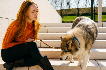 young beautiful red-haired girl walking with her dog in the park, sitting on a concrete staircase