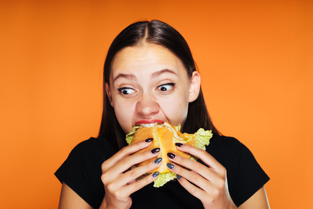 young beautiful girl wants to lose weight, but eagerly eats a harmful high-calorie hamburgerの写真素材
