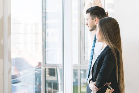 a young guy in a shirt and a long-haired girl in a suit waiting for someone and looking out the...