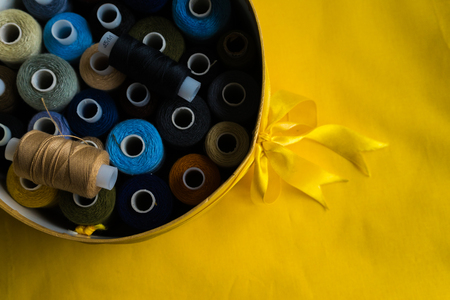 round box wrapped in a bow with coils of colored thread on a yellow backgroundの写真素材