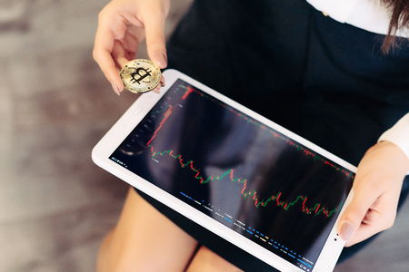 a girl with a tablet in her hands follows the course of a crypto currencyの写真素材