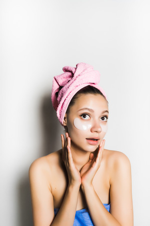 young beautiful girl with a pink towel on her head and silicone patches under her eyes, looking up thoughtfullyの写真素材