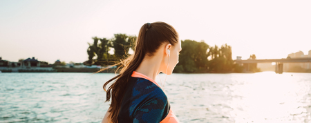 young sporty girl runs by the river at sunset, listens to music on headphonesの写真素材