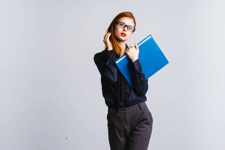 sexy red-haired girl with glasses and with red lips looking at the camera and holding a blue folder with documents, isolatedの写真素材