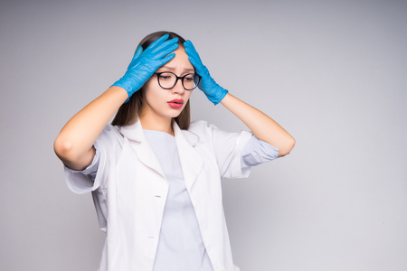 a girl in a medical gown and gloves and wearing big glasses holds her head in her hands and looks downの写真素材