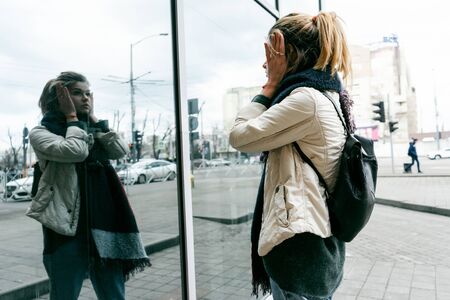 girl with a backpack on a city street looks at her reflection in the mirror