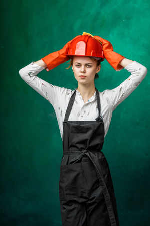 a young serious girl in an orange protective helmet and apron holds her head