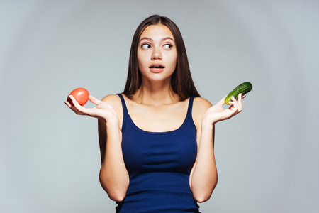 a young beautiful girl wants to lose weight, holds in her hand a useful tomato and cucumberの写真素材