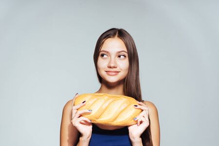 girl on a gray background holds a loaf in her handsの写真素材