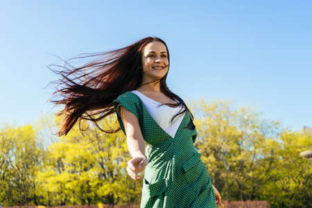 happy smiling girl with long dark hair in a green dress walking in the parkの写真素材