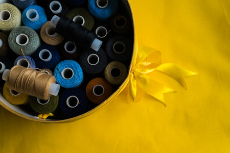 on a yellow surface in an iron bowl lie multicolored skeins of threadの写真素材