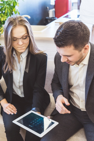 successful young guy and girl in suits sitting in office, looking at tabletの写真素材