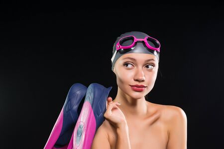 confident young woman swimmer in a swimming cap and glasses holding flippers and smilingの写真素材