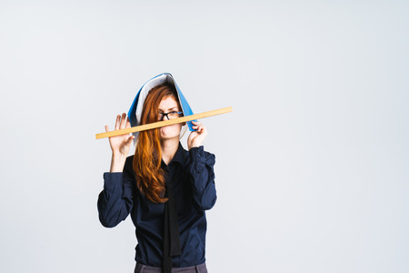 a strange red-haired girl with glasses, she has a folder on her head, holds a ruler near her mouthの写真素材