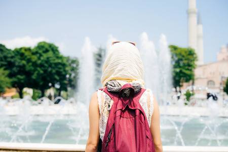 An unrecognizable woman in a scarf with a backpack on the background of a mosque and a fountain. Summer vacation, travelerの写真素材