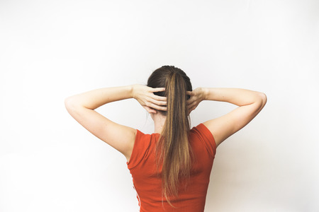 Woman back thinking isolated. a girl in a red T-shirt and with a tail stands behind and holds her hands behind her headの写真素材
