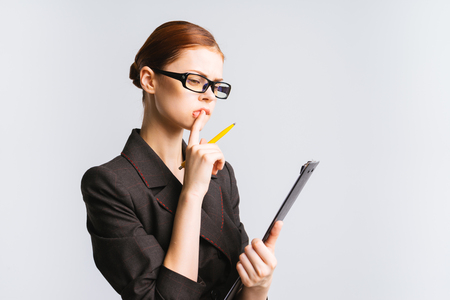 confident girl in a black suit and glasses looks at a notebook, thinks about something importantの写真素材