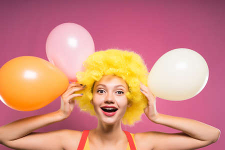 funny girl in a yellow clown wig laughs, holds in her hands colored balloonsの写真素材