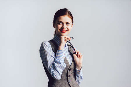 happy young girl with red lipstick and in strict clothes smiling, holding glasses in handsの写真素材