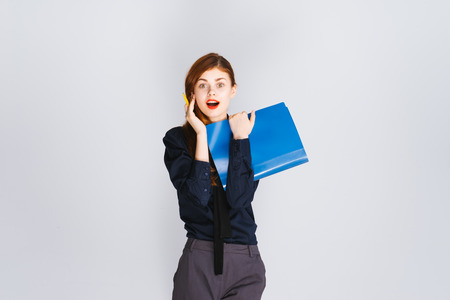 surprised stylish girl in dark clothes holding a folder with documents and looking at the cameraの写真素材