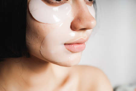 A young girl with black hair moisturizes her face with silicone patchesの写真素材