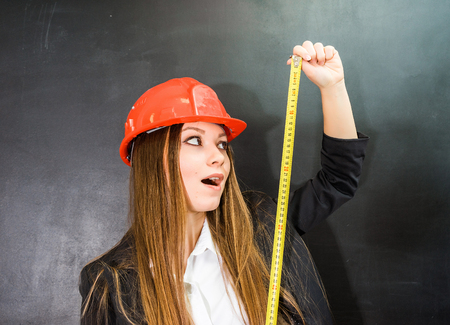 young surprised girl builder in a protective orange helmet holds a measuring tape in handの写真素材