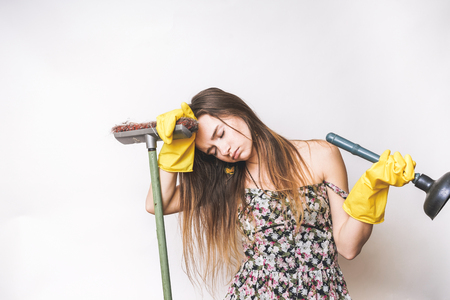 a tired young girl in yellow rubber gloves holds a plunger and a brush, is tired after cleaningの写真素材