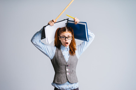 funny young schoolgirl in glasses looks sad and surprised, holds documents and ruler in handsの写真素材