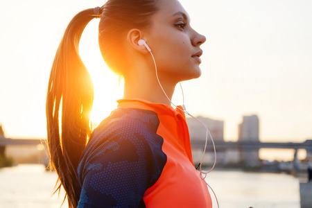 sports fitness girl listening to music in white headphones, in the sunの写真素材
