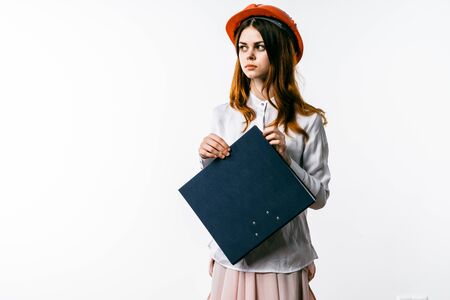 A girl secretary in a shirt and an orange construction helmet is holding a folderの写真素材